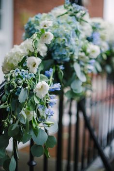 a bunch of blue and white flowers on a fence next to a brick building with black iron railings