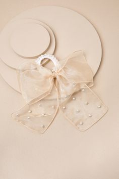 You don't need a reason to add a too-cute addition like the Lulus Darling Purpose Beige Organza Pearl Bow Ponytail Holder to your look! This adorable accessory starts with an elastic, white hair tie adorned with gleaming faux pearls, supporting a classic organza hair bow (with a subtle sheen and matching faux pearls throughout) that completes the balletcore-inspired design! Bow Measures 7. 5" Wide. Ribbon Measures 6" Long. 80% Polyester, 20% Acrylic. Imported. Lulus | Darling Purpose Beige Organza Pearl Bow Ponytail Holder. Bow Hair Tie, Bow Ponytail, Pearl Bow, Ponytail Holder, Bow Hair, Ponytail Holders, Hair Tie, White Hair, Hair Bow