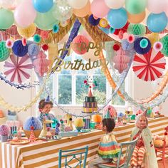 two children sitting at a table in front of a birthday party with balloons and streamers