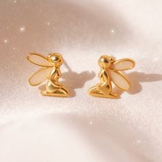 "Fairy Earrings - add a little magic with our adorable fairy stud earrings! Dainty matte gold stud earrings with shimmery fairy wings. Such a cute touch for your cottagecore or fairy dress fits! Wildflower + Co.Jewelry ♥ Measurements: dainty - a little under 1/2\"\" ♥ Materials: matte gold dipped metal & glitter enamel. Posts are titanium - good for sensitive ears! ♥ Packaged in our cute gift box ♥ Designed by & exclusive to Wildflower + Co. ♥ Imported ♥ Product safety - intended for use by adul Gold Fairy Earrings For Gift, Gold Fairy Style Handmade Earrings, Handmade Gold Fairy Earrings, Gold Handmade Fairy Earrings, Fairycore Earrings For Pierced Ears As A Gift, Earrings Fairycore, Jewelry Measurements, Fairy Earrings, Fairycore Fairy