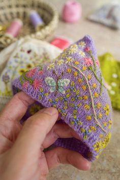 a hand is holding a purple crocheted pillow with flowers and vines on it