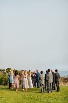 a group of people standing on top of a lush green field next to the ocean