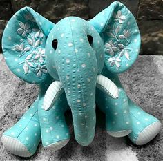 an elephant stuffed animal sitting on top of a carpet next to a stone wall with white polka dots