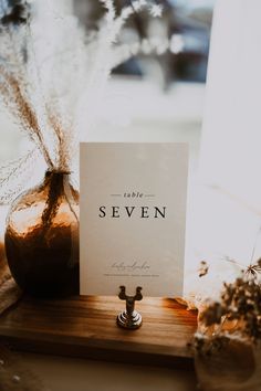 a card is sitting on a table next to a vase with dried flowers in it