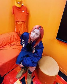 a woman with red hair sitting on the floor next to a bed and orange walls