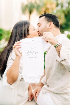 a man and woman kissing while holding up a t - shirt