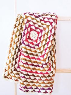 a multicolored crocheted blanket hanging on a wall