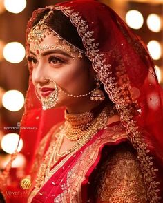 a woman wearing a red and gold bridal outfit with jewelry on her face, smiling at the camera