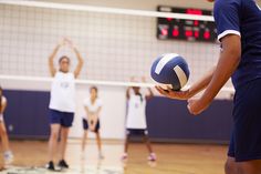 a group of young people playing volleyball in a gym with one person holding the ball