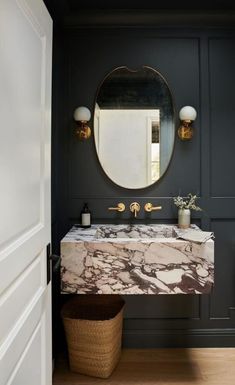 a bathroom sink with marble counter top and gold faucet, along with a round mirror above it