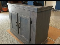 a wooden cabinet sitting on top of a floor next to a black dog laying in the background