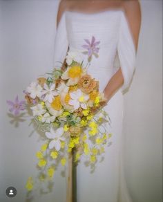 a woman in a white dress holding a bouquet of yellow and white flowers on her wedding day