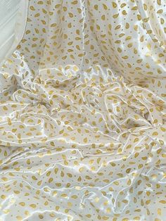 an unmade bed with white sheets and gold leaf print on it's cover