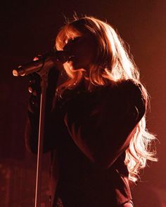 a woman singing into a microphone in front of a dark stage with lights behind her