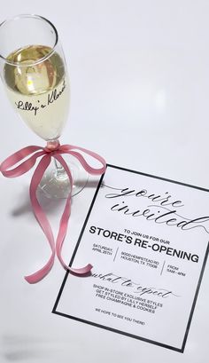 a glass of wine sitting on top of a table next to a card with the words store's re - opening