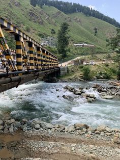 there is a yellow and black bridge over the river that goes under it with rocks on both sides