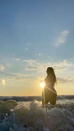 a woman standing in the ocean at sunset