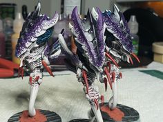 two alien warhammers with purple and white paint on their bodies, standing on red bases