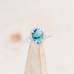 a ring with a blue stone in the center on top of a wooden stand,