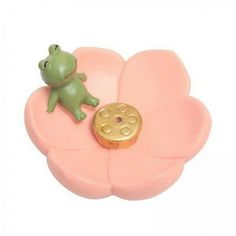 a toy frog sitting on top of a pink flower shaped object with a gold disc