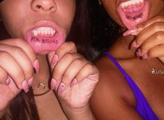 two women with fake teeth are holding their mouths open and one has writing on her tongue