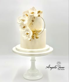 a white and gold wedding cake with flowers on the top is sitting on a pedestal