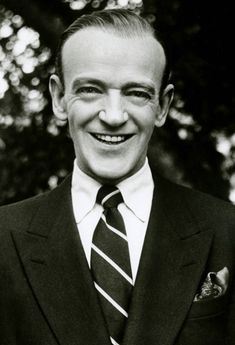 a man in a suit and tie smiling at the camera with trees in the background