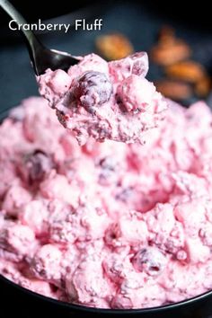 a spoon full of cranberry fluff on top of a black bowl filled with blueberries