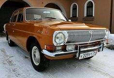 an orange car parked in front of a brown building with snow on the ground around it