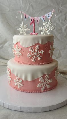 a three tiered cake with pink frosting and white icing snowflakes