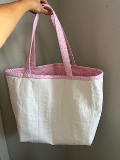 a person is holding a pink and white tote bag in front of a gray wall