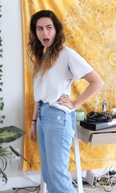 a woman standing in front of a wall with her hands on her hips and looking surprised