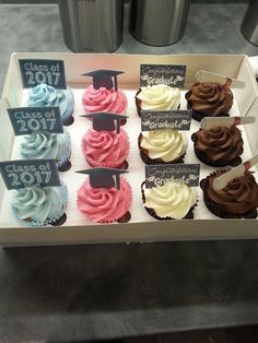 cupcakes with graduation decorations on them are displayed in a display case for sale