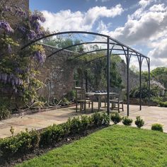 an outdoor dining area in the middle of a garden with purple wisters growing on it