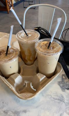 three iced coffees are sitting on a tray with straws in each cup and one is empty