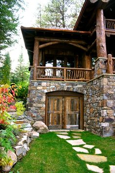 a house made out of rocks and wood in the middle of some grass with stepping stones leading up to it