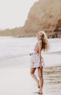 a woman standing on top of a sandy beach next to the ocean with her hair blowing in the wind