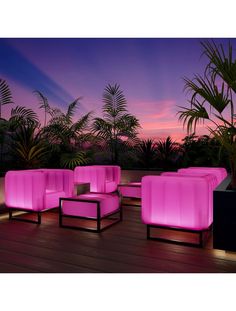 pink couches and chairs on a wooden deck at dusk with palm trees in the background