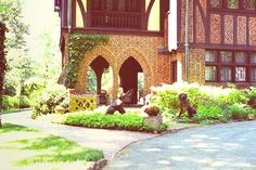 an old house with flowers in the front yard and statues on the sidewalk near it