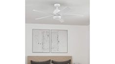 a white ceiling fan mounted above a bed in a room with two paintings on the wall