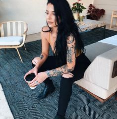 a woman sitting on the floor with tattoos on her arm and leg, holding a purse