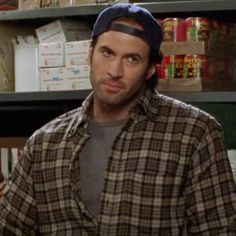 a man in a plaid shirt and hat standing in front of shelves