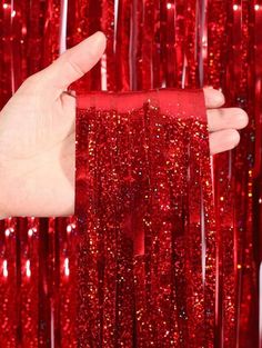 a hand is holding a red ribbon in front of some sequinized foil curtains