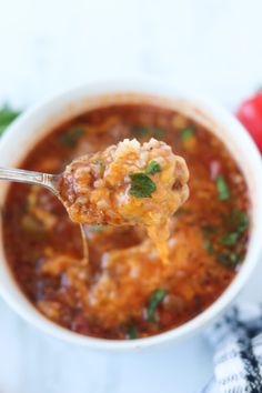 a spoon full of chili soup with cheese and parsley on the side, ready to be eaten