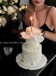 a woman sitting in front of a cake with a lit candle on top of it