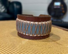 "One of a kind, upcycled leather bracelet made from used belts, upholstery scraps, and artistic findings. Every cuff is unique and made to wear and weather well.  Like high quality boots or your favorite leather journal, these cuffs get softer and more supple over time. The individual designs all start with the leather.  I use vintage belts, leather scraps, WW2 rifle holsters, and old horse bridles.  Each piece speaks to me, and informs the direction for the finished piece.  Adornments include found objects, printed leather, metal studs, gemstones, buttons - anything that will bring the cuff to life and make it a statement piece unlike any other. I prefer using a button & elastic closure when possible, as it makes the cuff fully adjustable.  It's a more labor and cost intensive process, bu Unique Leather Cuff Bracelet With Strap, Adjustable Leather Cuff Bracelet Hand-stitched, Rustic Leather Bracelet For Festivals, Handmade Artisan Leather Bracelet, Adjustable Hand-stitched Leather Cuff Bracelet, Rustic Handmade Leather Cuff Bracelet, Unique Handmade Leather Cuff Bracelet, High Quality Boots, Horse Bridle