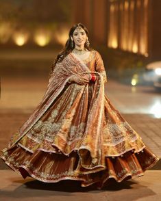 a woman in an orange and gold lehenga is walking down the street at night