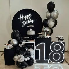 a table with black and white balloons, silver and black decorations and a happy birthday sign