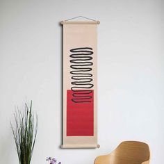 a wooden chair sitting in front of a white wall with a red and black painting on it