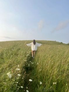 a woman walking through tall grass towards the sky